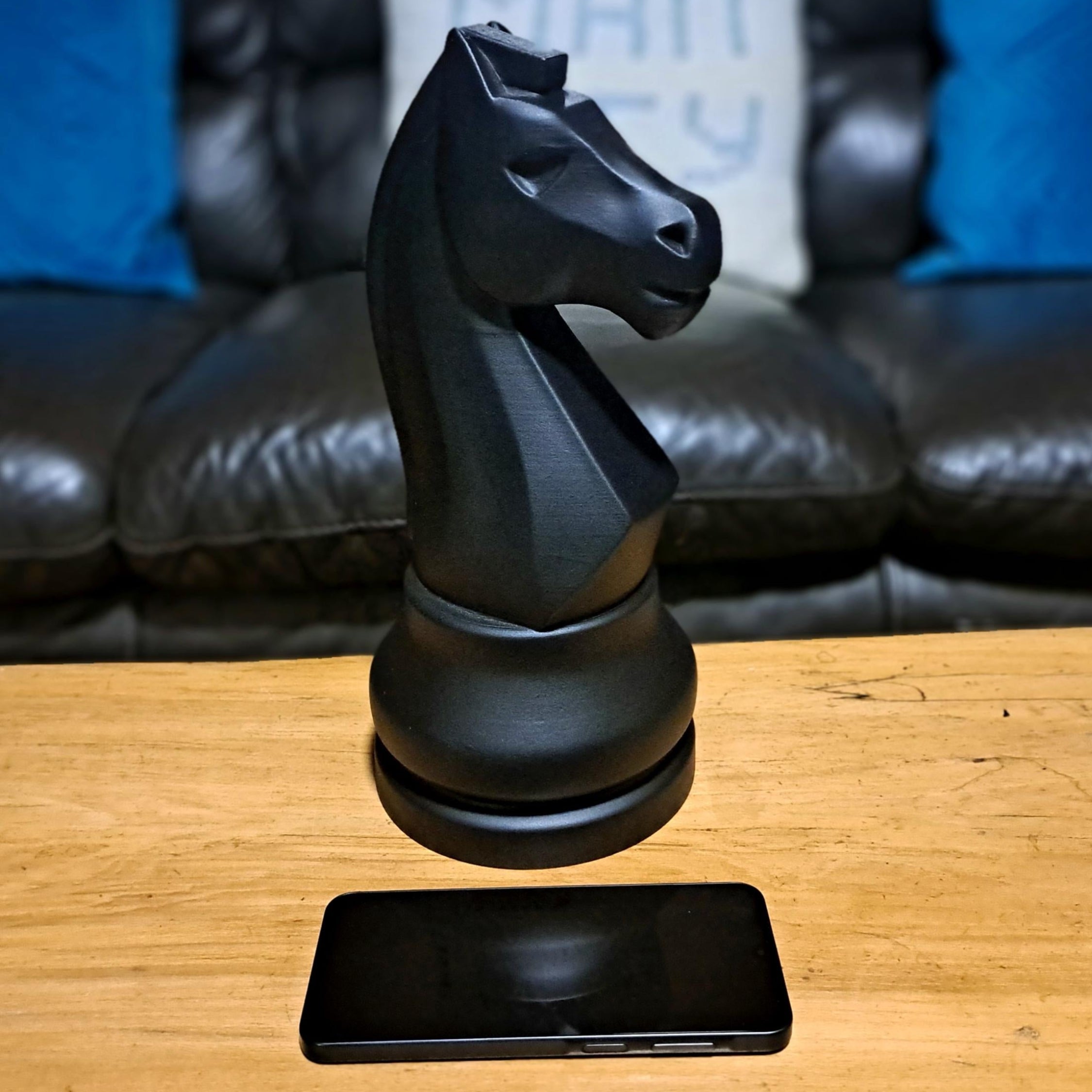 Black knight chess piece with a smartphone on a wooden surface with a sofa in the background.