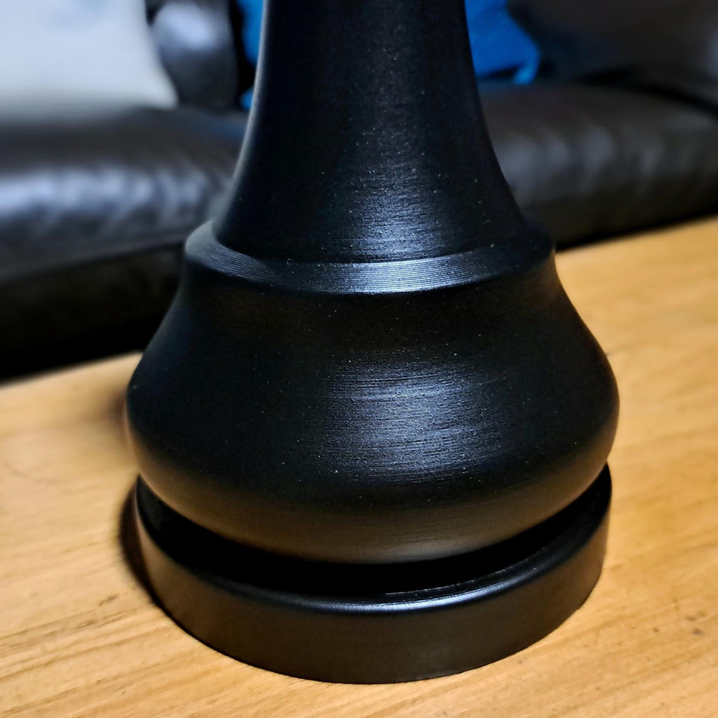 Close up shot of a large black king chess piece on a wooden surface with a sofa in the background