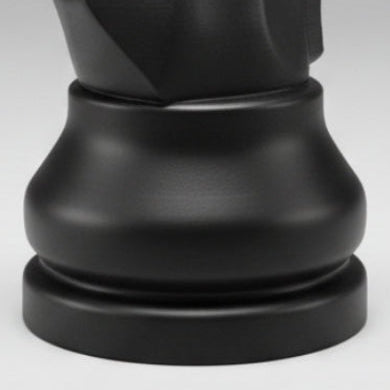 A matte black chess knight piece,standing  against a neutral gray studio background.