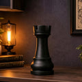Large decorative rook chess piece on a wooden shelf with a lamp and plants in a dimly lit room.