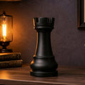 Large decorative rook chess piece on a wooden shelf with a lamp and plants in a dimly lit room.