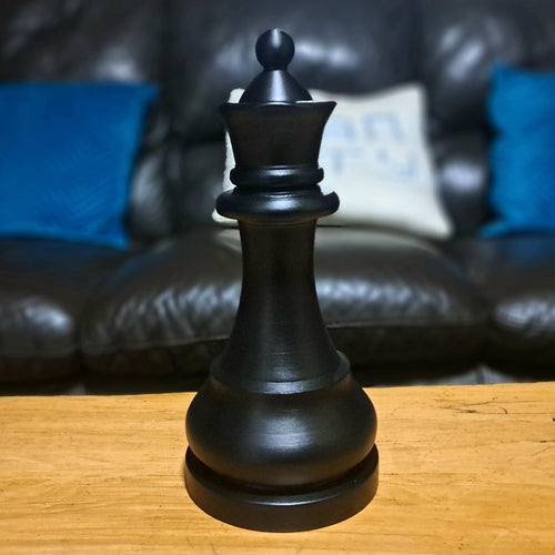 Black queen chess piece on a wooden surface with a blurred sofa in the background