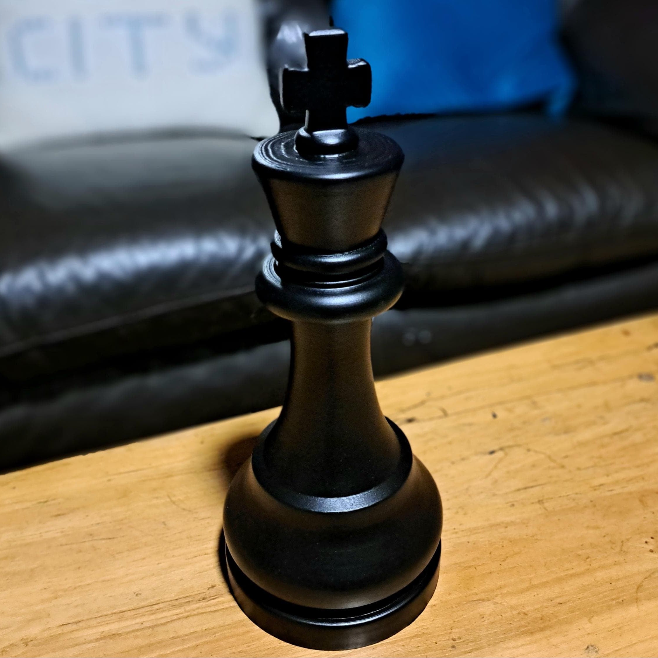 Large black king chess piece on a wooden surface with a sofa in the background