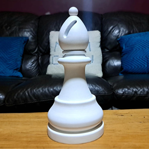 Large white bishop chess piece on a wooden table with a dark leather sofa and blue cushions in the background.