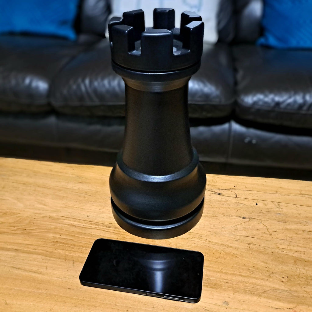 Large black rook chess piece on a wooden surface with a sofa in the background