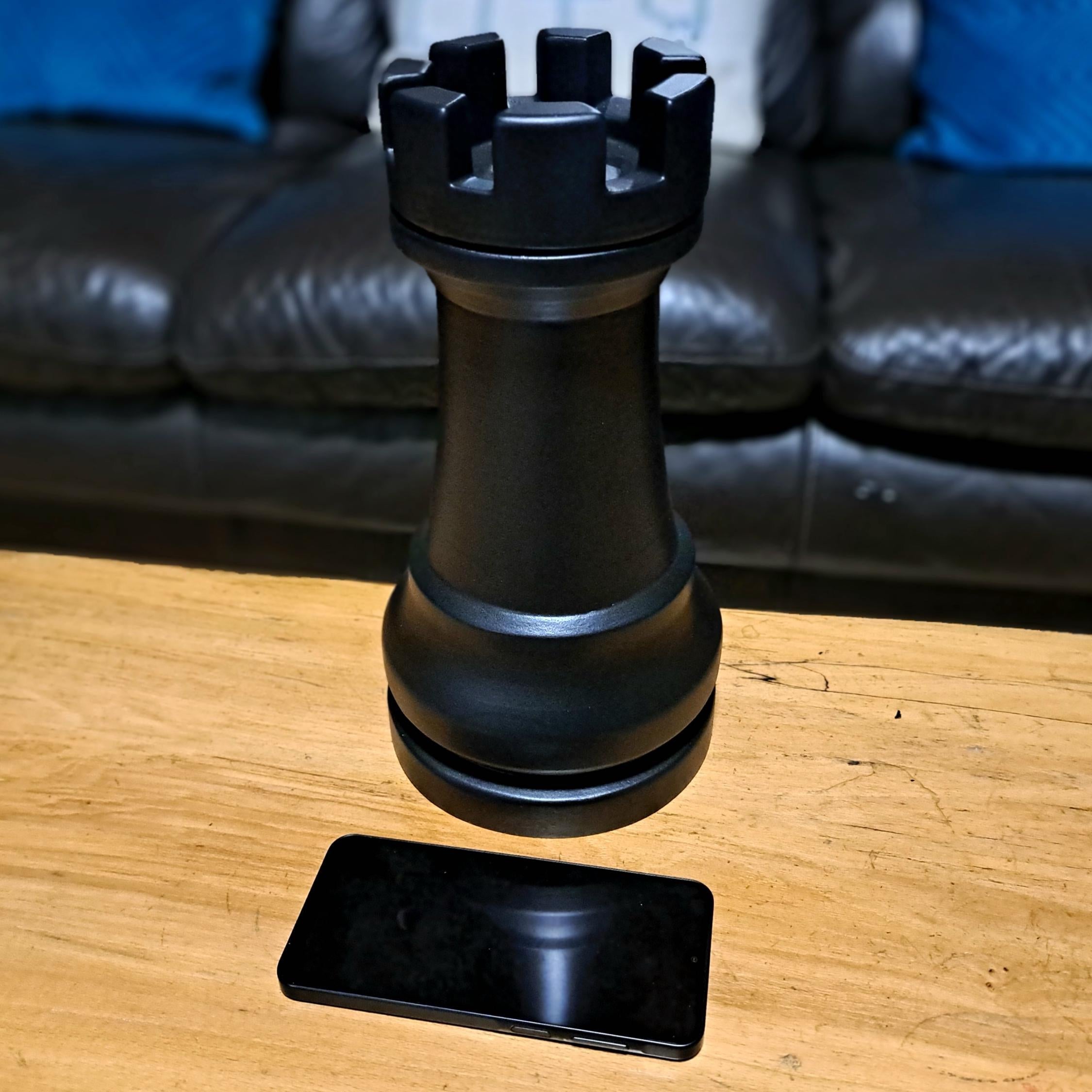 Large black rook chess piece on a wooden surface with a sofa in the background
