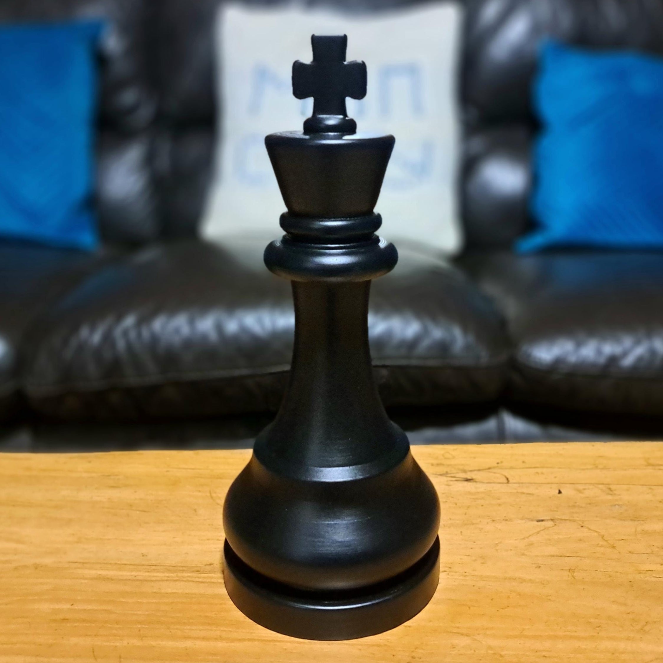 Large black king chess piece on a wooden table with a sofa in the background