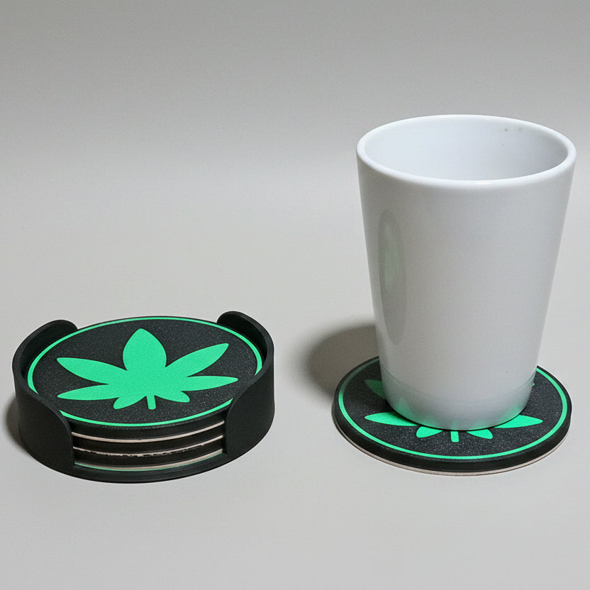 Set of four coasters with green leaf design on a grey surface, one coaster with a white cup.