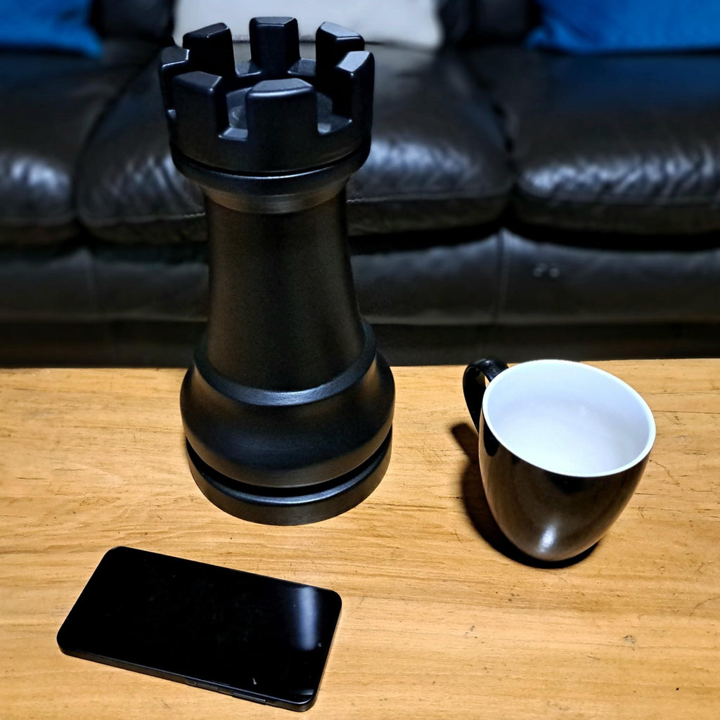 Large black rookchess piece, a mug, and a smartphone on a wooden table with a dark sofa in the background.