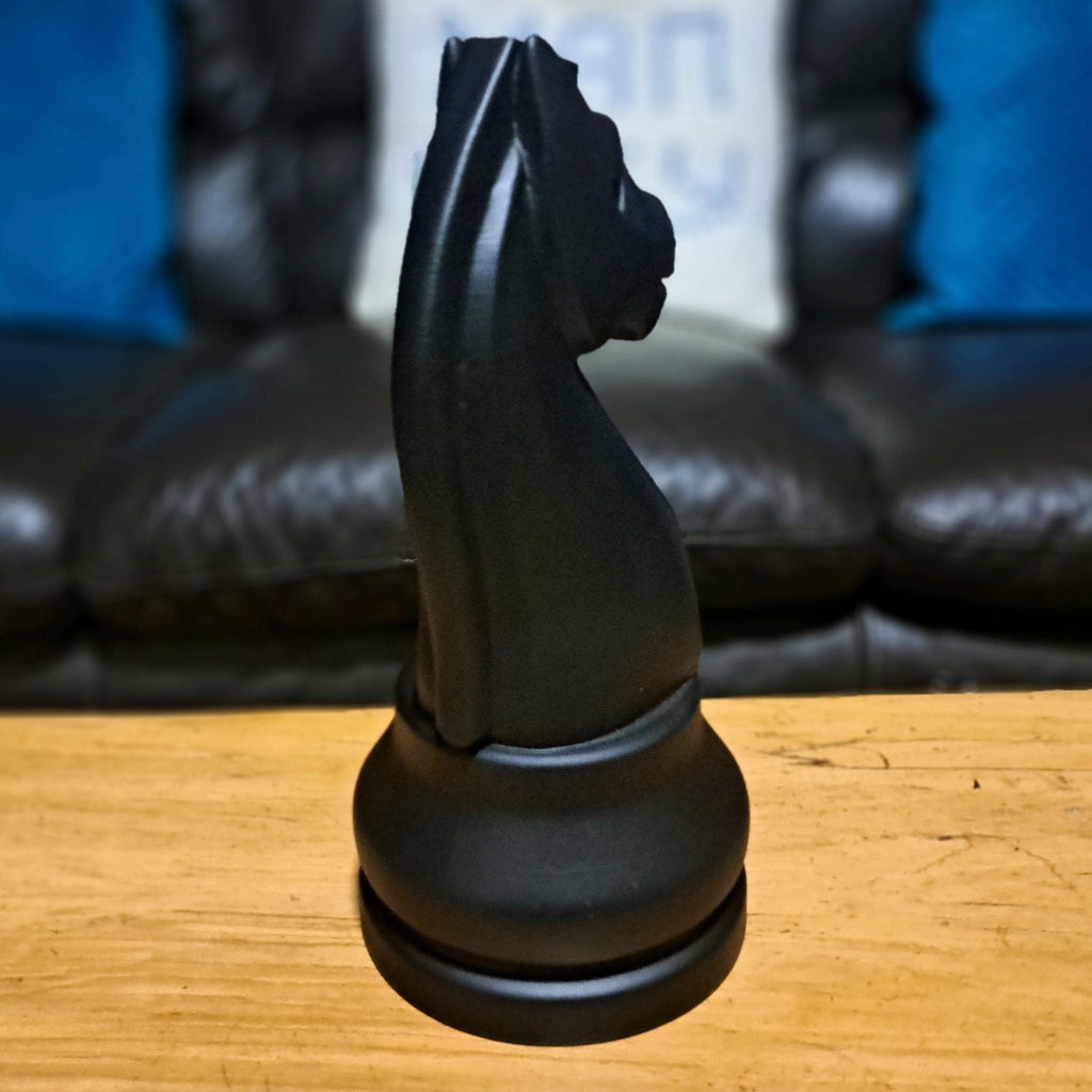 Large black knight chess piece on a wooden table with a sofa in the background
