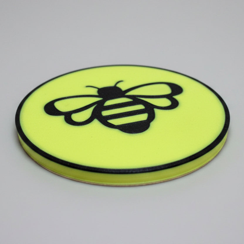 Close up shot of a yellow and black bee coaster on a grey background.