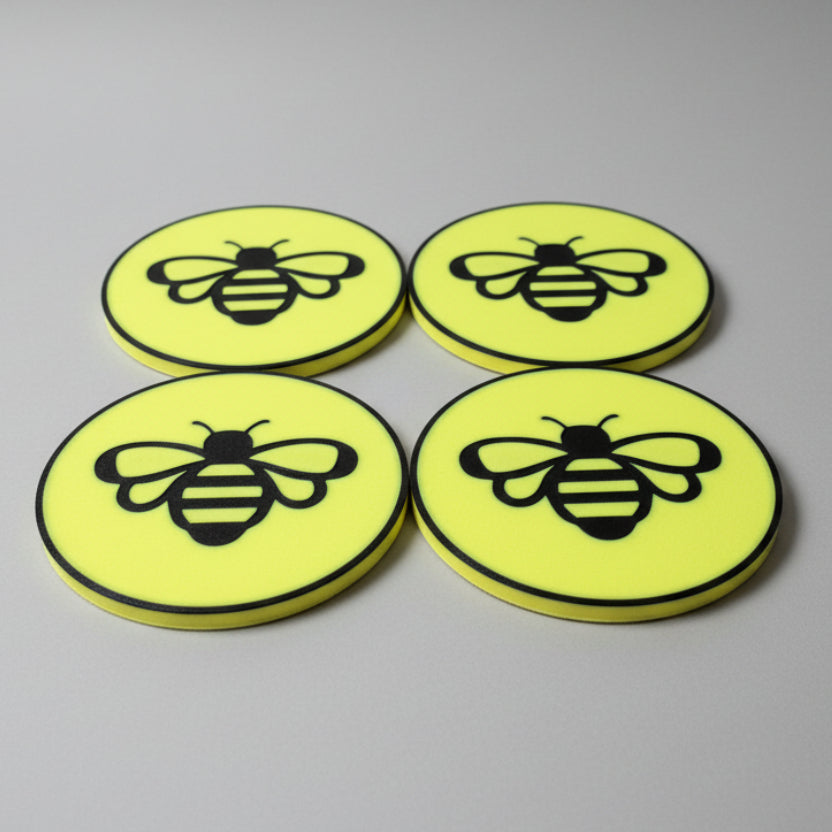 Four yellow coasters with bee design on a grey background.