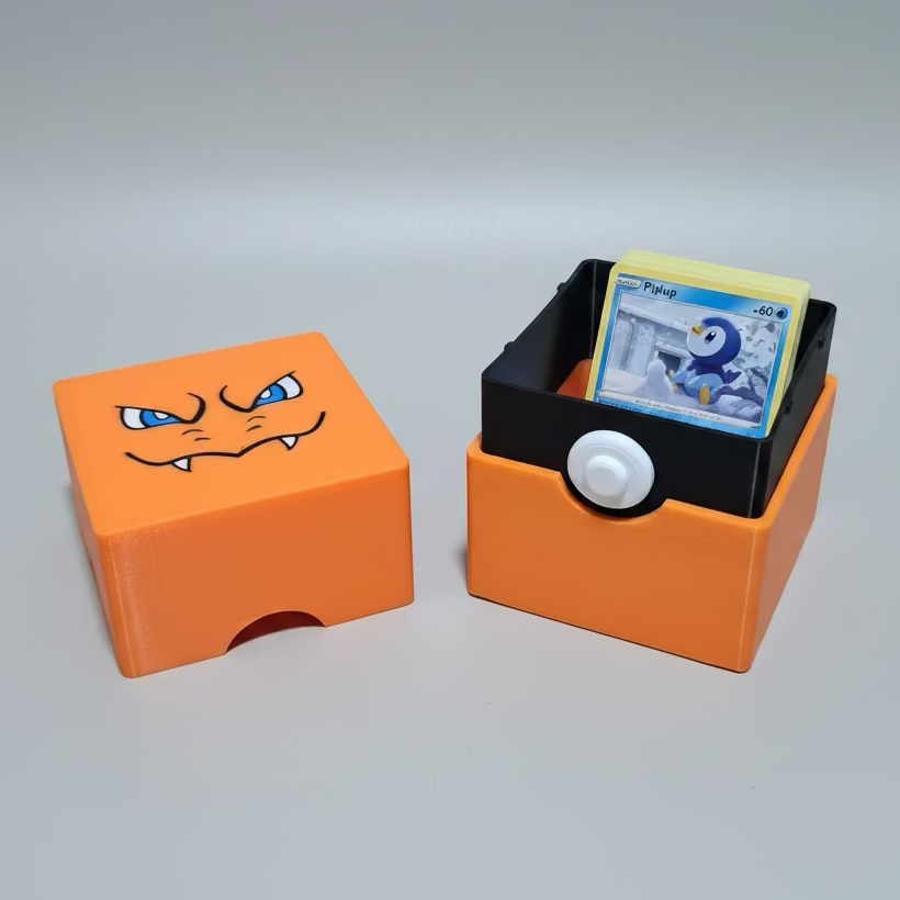 An orange and black 3D-printed Charizard-themed card holder with its lid placed beside it. The lid features a printed Charizard face, and the holder contains a Pokémon card.