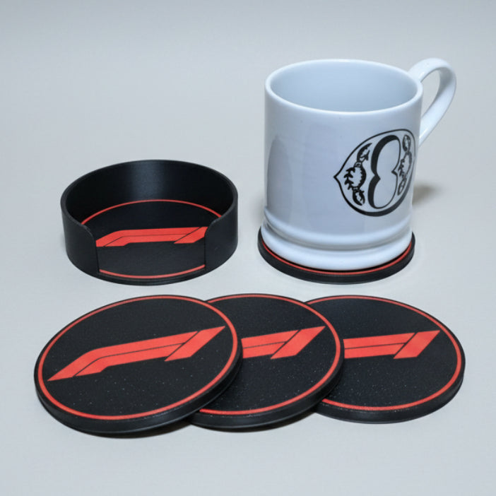 Four black and red F1-themed coasters and a matching holder alongside a white ceramic mug on a grey background.