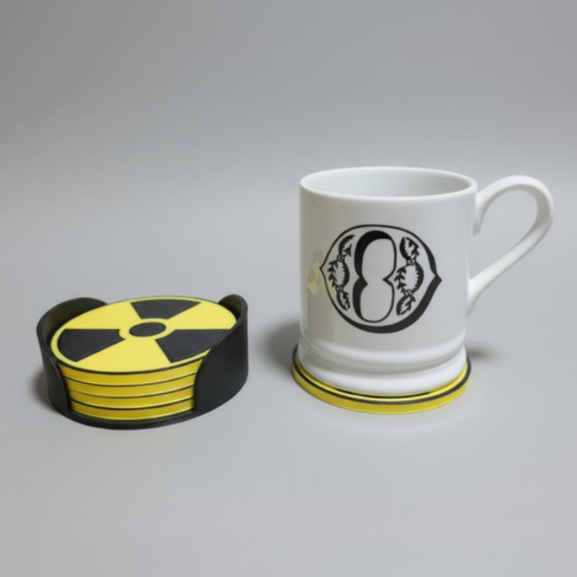White mug on a grey background next to yellow and black coasters.