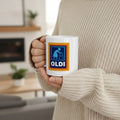 A person in a beige knit sweater holds a white ceramic mug with a blue and yellow graphic that reads 'OLDI' and shows an icon of an elderly person using a walker.