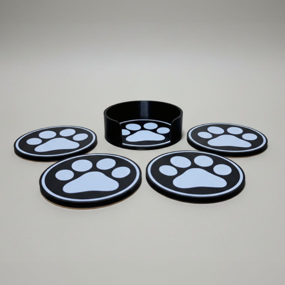 Four black and white paw print coasters on a grey background.