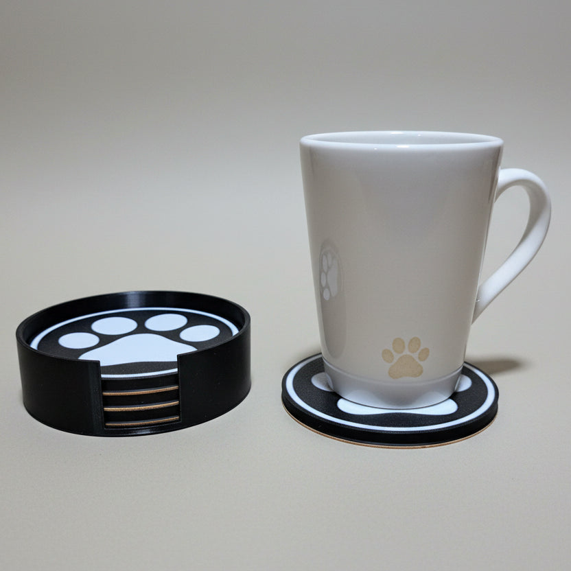 White mug on a set of black coasters with paw prints on a grey background.