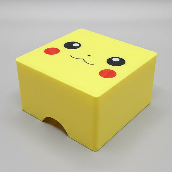 Top-down view of 3D printed Pikachu Pokémon deck box in bright yellow, showing Pikachu face lid artwork with black eyes, red cheeks and smile, and front thumb notch cutout.