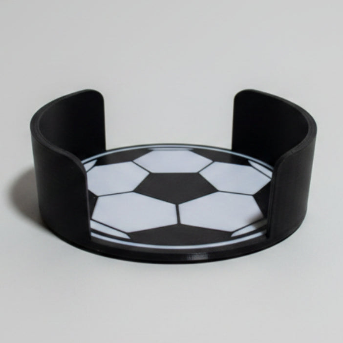Soccer ball design on a black coaster holder on a grey background.