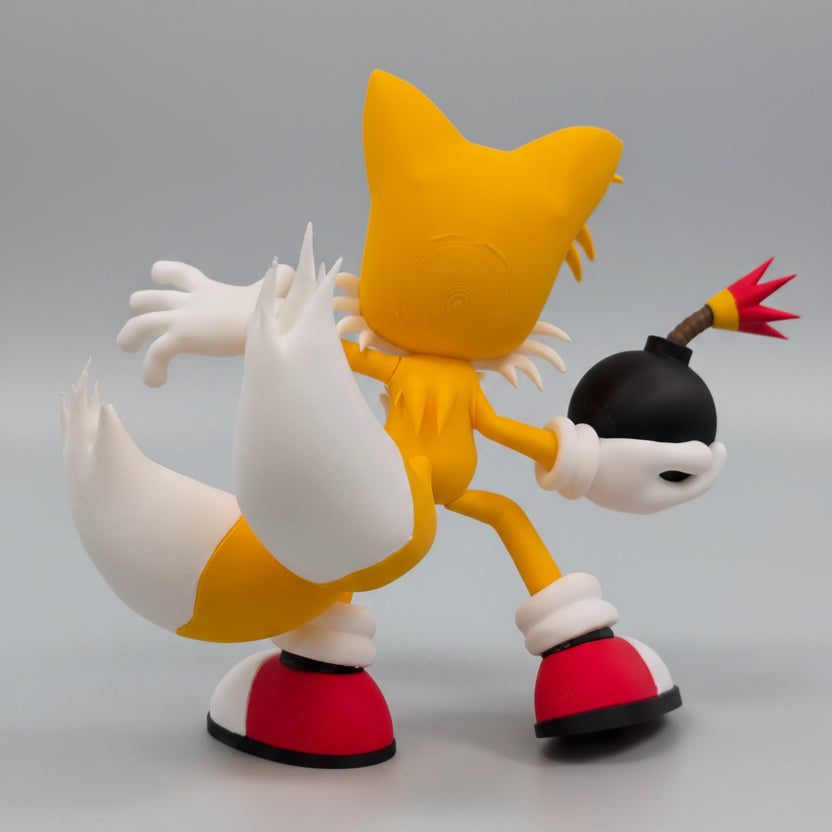 Tails  with yellow fur, white chest, and red shoes holding a black bomb on grey background.