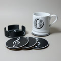 White mug and black coasters with white music notes on a grey background.