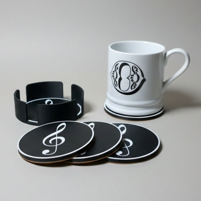 White mug and black coasters with white music notes on a grey background.