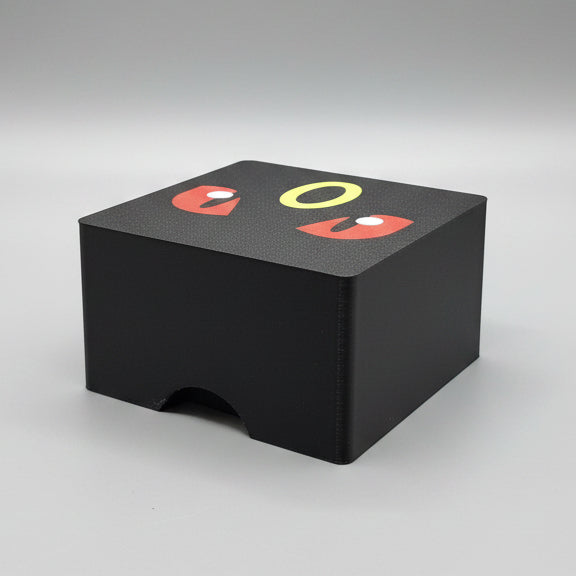 Top-down view of 3D printed Umbreon Pokémon deck box in matte black, showing Umbreon face lid artwork with red eyes and yellow ring, and front thumb notch cutout.