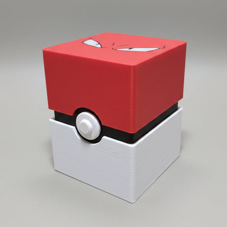 3D printed Poké Ball-style trading card deck box closed, red angry-eyes lid on white base with button detail, lifestyle shot on wooden table.