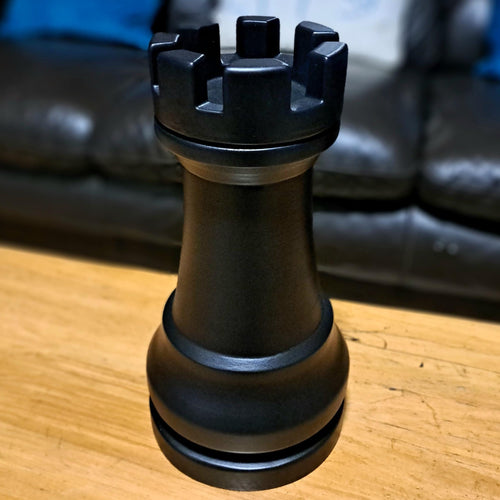 Large black rook chess piece on a wooden table with a sofa in the background
