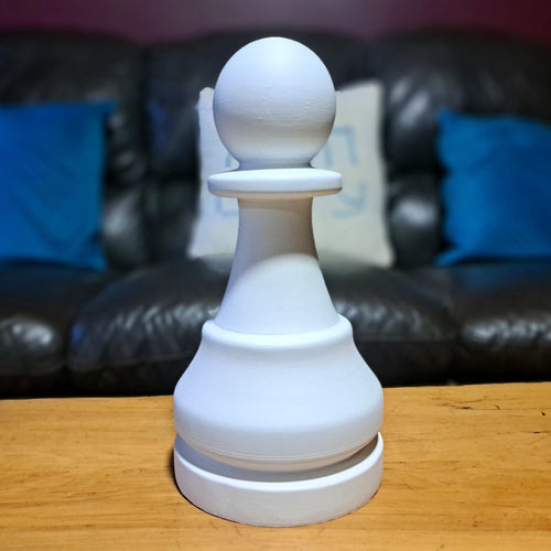 White pawn chess piece on a wooden surface with a sofa and pillows in the background