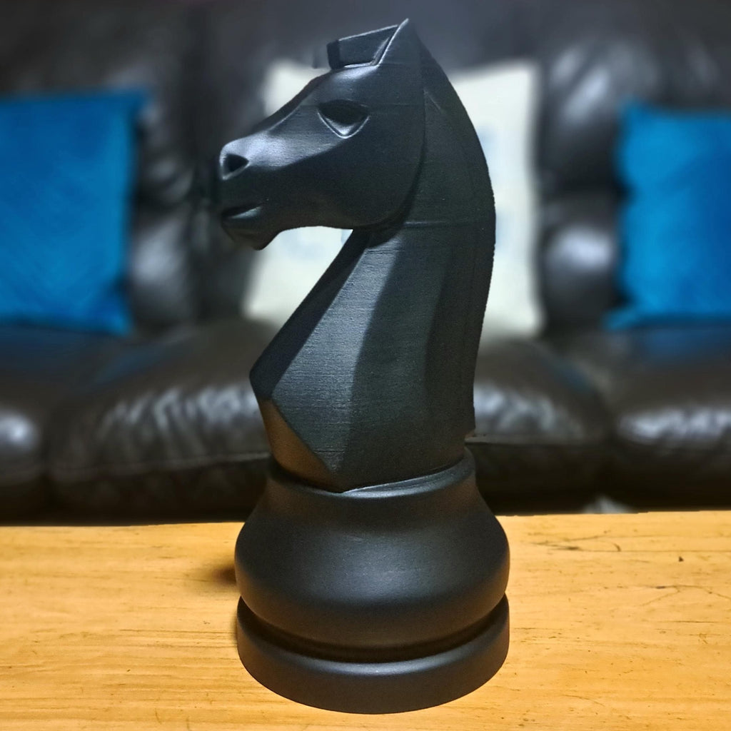 Large black knight chess piece on a wooden surface with a sofa in the background