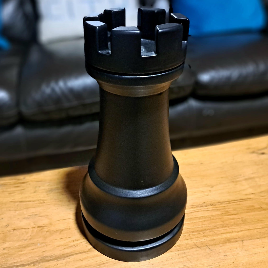 Large black rook chess piece on a wooden table with a sofa in the backgorund